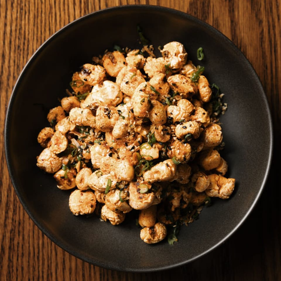 A black bowl filled with crispy popcorn chicken, garnished with green onions and sesame seeds.