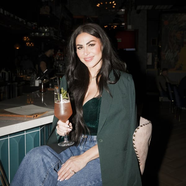 A woman in a green top and blazer sips a cocktail at the Dodo Bird Kitchen and Cocktails bar.