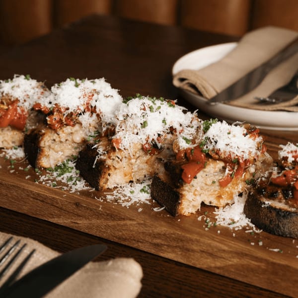Toasted bread slices topped with red sauce, white cheese, and green herbs on a wooden board.