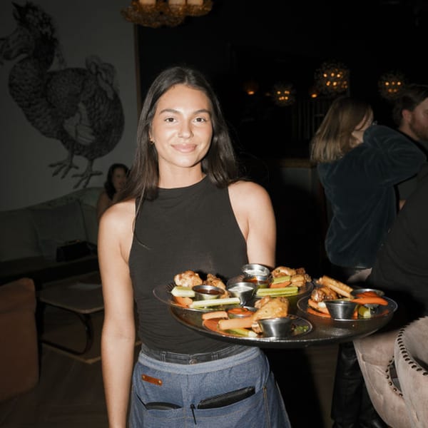 Smiling server holding a tray of Dodo Bird Kitchen and Cocktails' wings and appetizers.