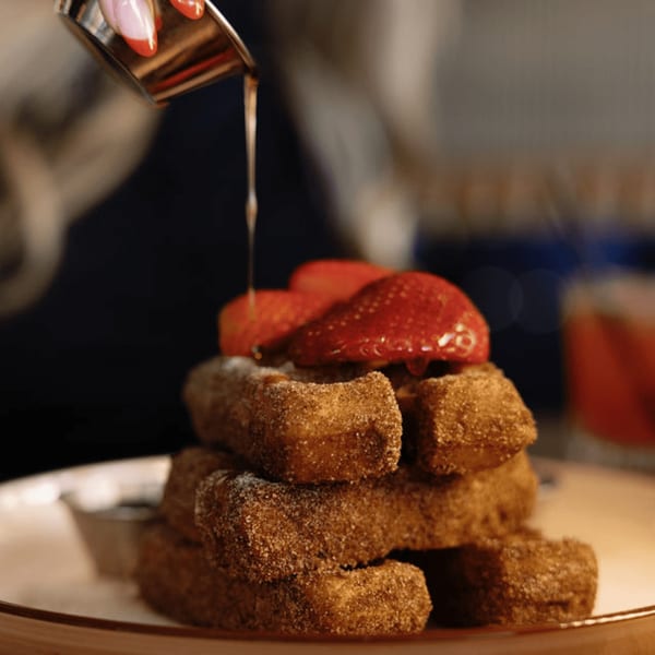 Maple syrup being poured over Dodo Bird Kitchen's cinnamon sugar churro fries topped with strawberries.
