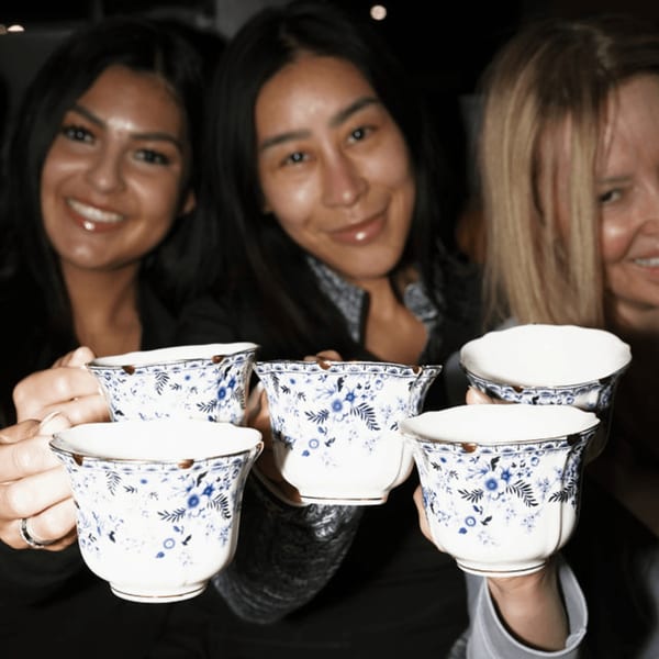 Three smiling women holding up ornate blue and white teacups, possibly for cocktails at Dodo Bird Kitchen.