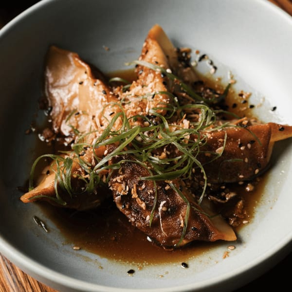 Dodo Bird Kitchen and Cocktails' dumplings in sauce, garnished with green onions and sesame seeds.