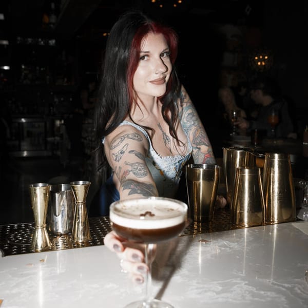 Bartender with tattoos serving an espresso martini at Dodo Bird Kitchen and Cocktails.