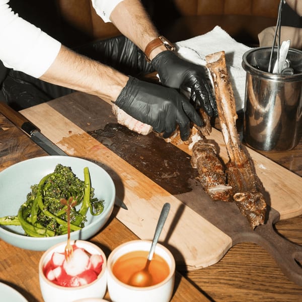 Chef in black gloves carving a large bone-in rib roast on a wooden board, with sides.