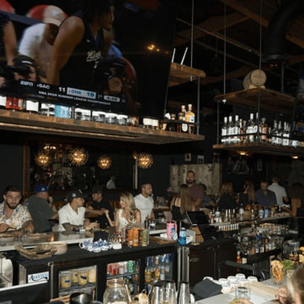 Patrons enjoying drinks and watching sports on a large screen at Dodo Bird Kitchen and Cocktails bar.