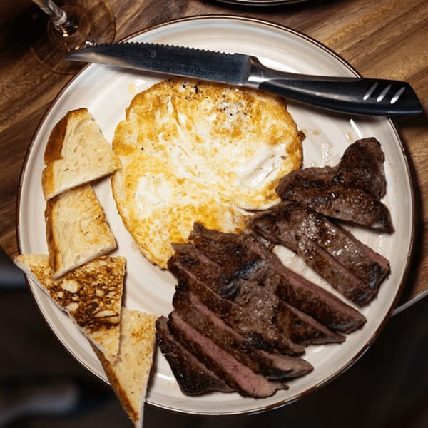 A plate of sliced steak, a fried egg, and toasted bread, with a knife resting on top.