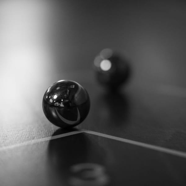 Two shiny, dark marbles on a surface with a faint number '3' and a white line.