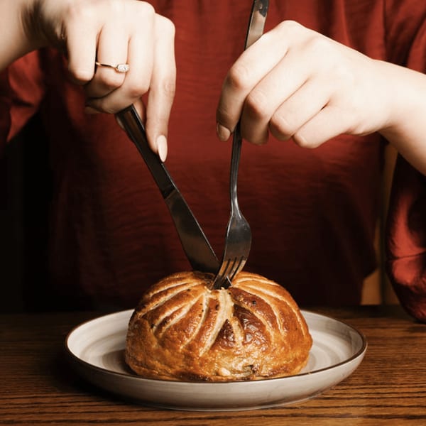Hands cutting into a golden-brown, dome-shaped pastry dish on a white plate at Dodo Bird Kitchen.