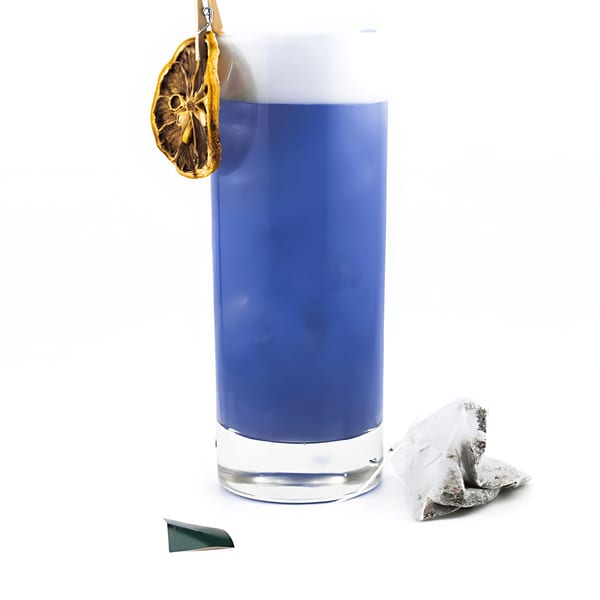 A tall glass of vibrant blue cocktail, garnished with a dried lemon slice and a tea bag.